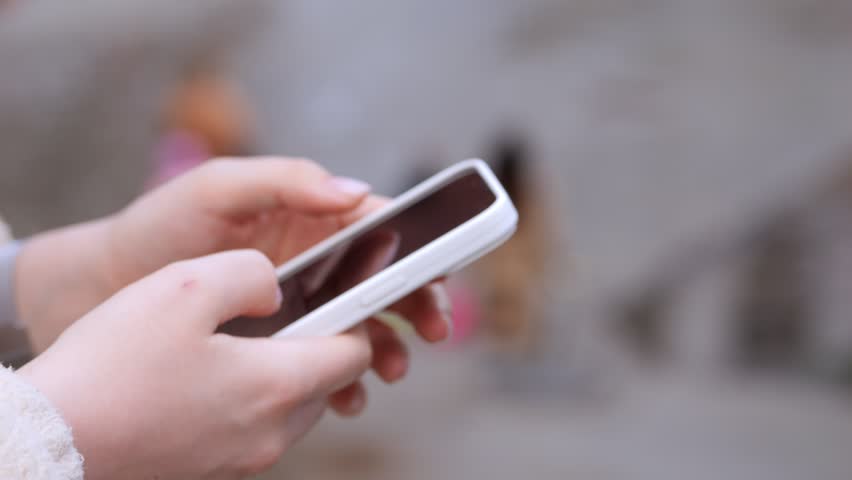 Close-up of hands using a smartphone outdoors. Blurred background shows people walking. Calm, focused, everyday digital interaction. Ideal for mobile apps, communication, or urban lifestyle content