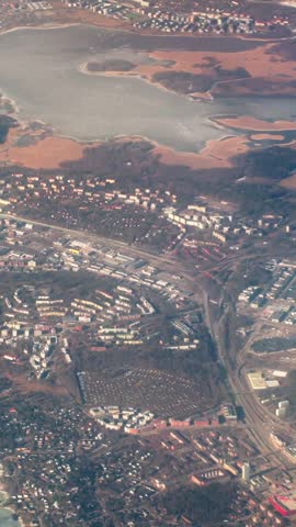 Aerial view of Helsinki with urban districts, road network, industrial areas, and coastal wetlands, captured from an airplane during descent in warm evening light.
