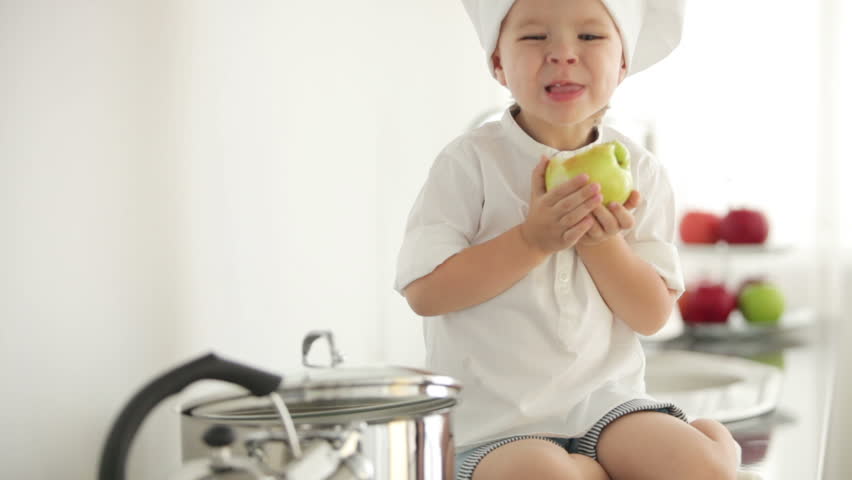 Chef boy eating apple in kitchen and smiling
