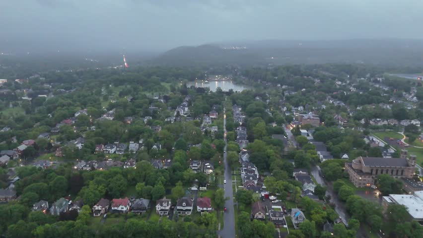 Moving over a neighborhood and towards a pond in the distance as the backdrop appears to showcase large rolling hills cloaked in fog.