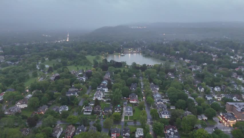Moving over a neighborhood and towards a pond in the distance as the backdrop appears to showcase large rolling hills cloaked in fog.