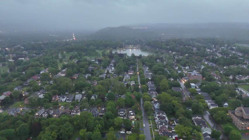 Moving over a neighborhood and towards a pond in the distance as the backdrop appears to showcase large rolling hills cloaked in fog.