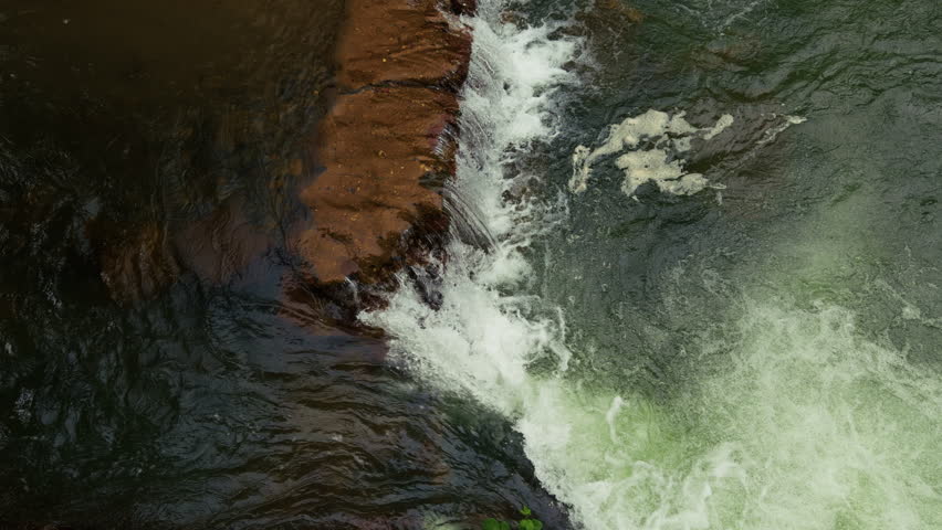 Wide scenic shot of a powerful waterfall cascade flowing into a rocky river bed with fresh water streaming over large wet stones and boulders in a crisp high fidelity beautiful natural mountain landscape texture