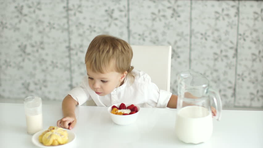Boy sitting at table and in front of him yogurt, milk and cake
