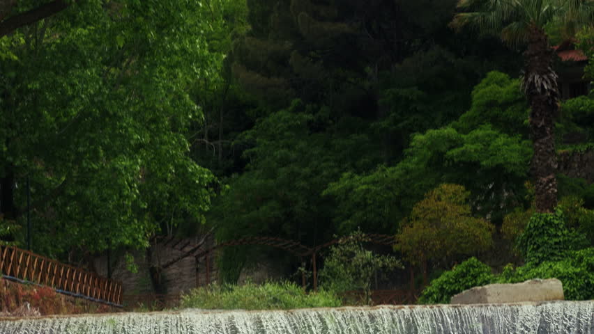 Wide scenic shot of a powerful waterfall cascade flowing into a rocky river bed with fresh water streaming over large wet stones and boulders in a crisp high fidelity beautiful natural mountain landscape texture