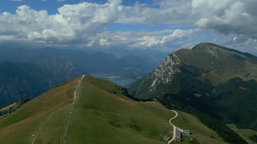 Aerial view of grassy mountain ridge with winding trail overlooking distant lake