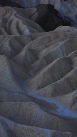 Vertical Screen: Eroded mudstone badlands at Zabriskie Point in Death Valley National Park California during blue hour twilight with dramatic ridges and sedimentary rock formations creating waves.