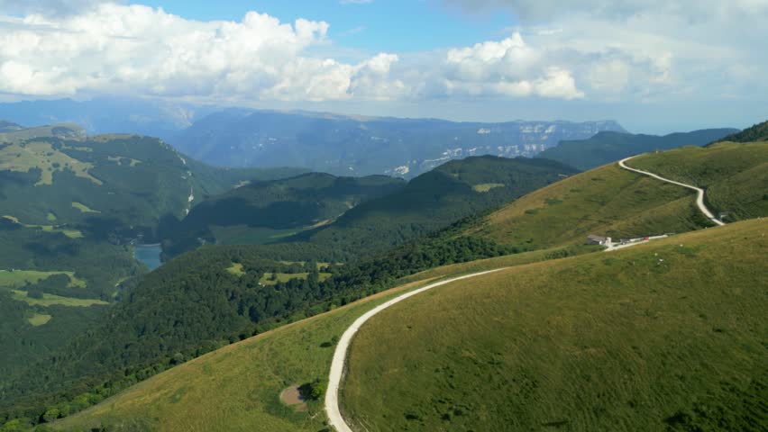 Curving mountain road runs along grassy ridges above lake and forested slopes