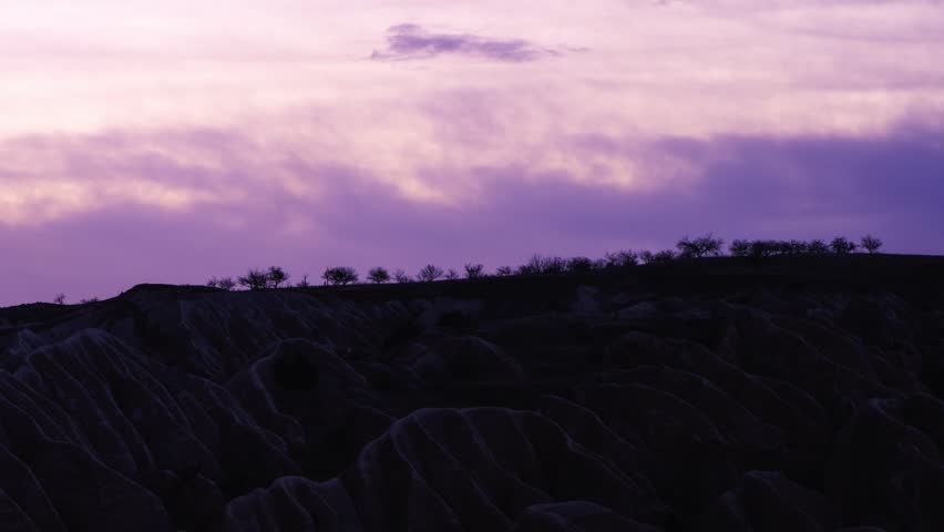 Purple evening sky over dark rocky hills and rugged natural formations.