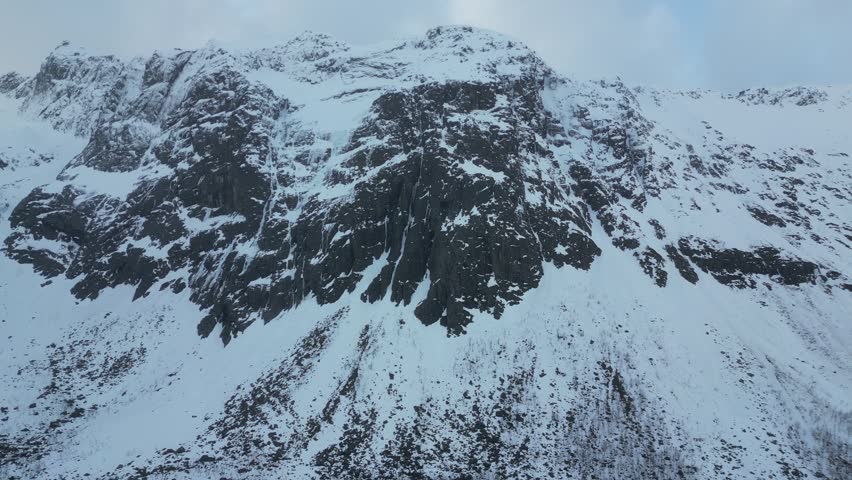 Aerial view of the snowy mountain peaks and rugged dark rock faces of Grotfjorden, Troms, Norway.