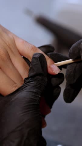 Close-up of nail technician pushing back cuticle with orange stick. Professional manicure service, nail preparation, beauty salon treatment and precise hand care.