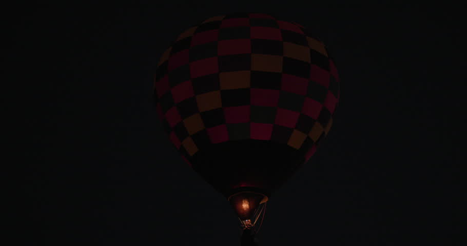 Real-time footage of a hot air balloon burner firing mid-flight, illuminating a Dawn Patrol balloon against the dark early morning sky during the 2025 Albuquerque International Balloon Fiesta in Albuquerque, New Mexico. Dramatic burner flame and glowing balloon create a vivid pre-sunrise aviation scene ideal for travel, event, and cinematic storytelling.