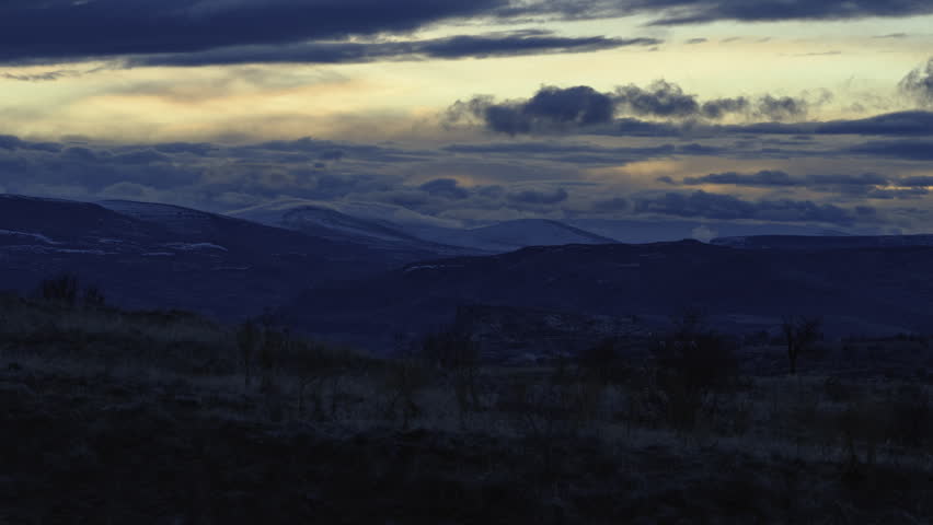 Wide sunset landscape with dark hills and glowing clouds over the horizon.