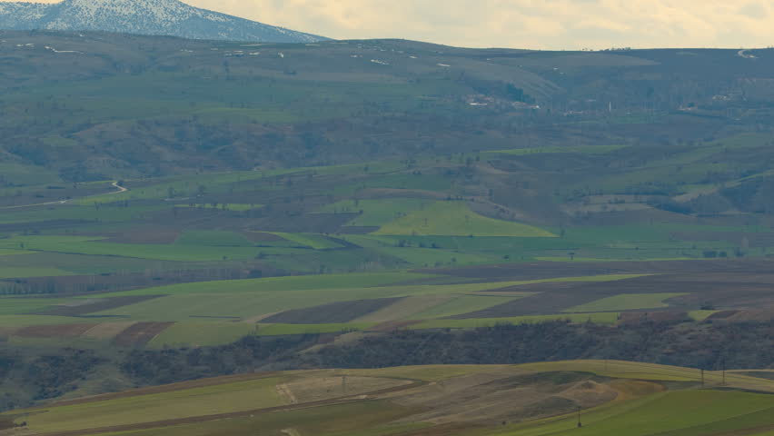 Wide rural landscape with green fields, rolling hills, and distant mountains.