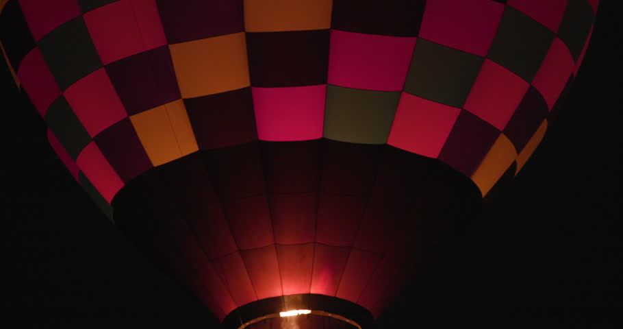 Close-up real-time footage of a hot air balloon burner firing and illuminating the lower envelope of a balloon against the dark night sky during the 2025 Albuquerque International Balloon Fiesta in Albuquerque, New Mexico. Dramatic flame and glowing fabric create cinematic aviation footage ideal for travel, event, and storytelling use.
