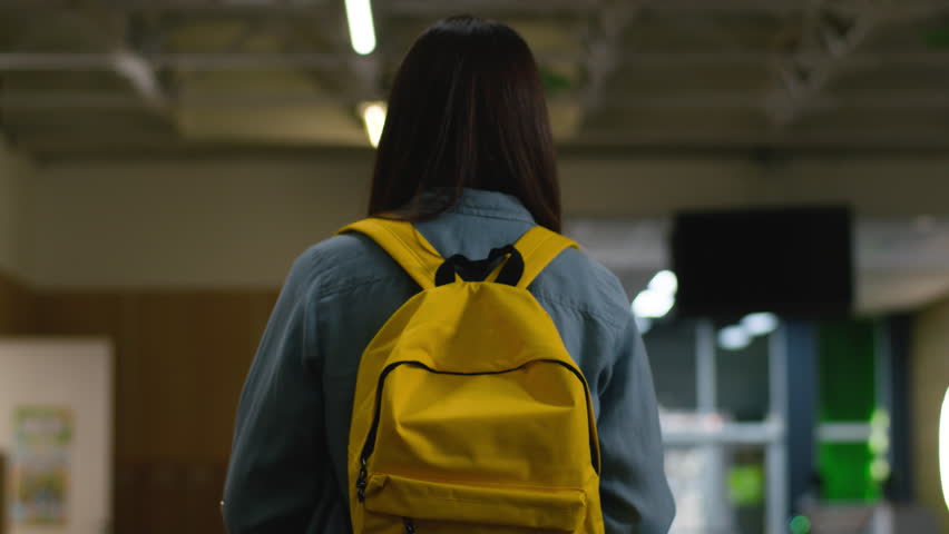 Back view unrecognizable girl teenager student with schoolbag walking in school corridor woman brunette female walk going to classroom move to lesson education pupil academy university college study