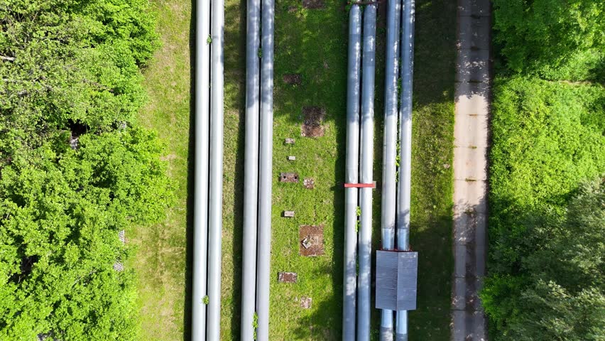 Aerial view of industrial pipes for gas, water, and oil running parallel across a green landscape, showcasing a continuous flow of infrastructure and nature in harmony