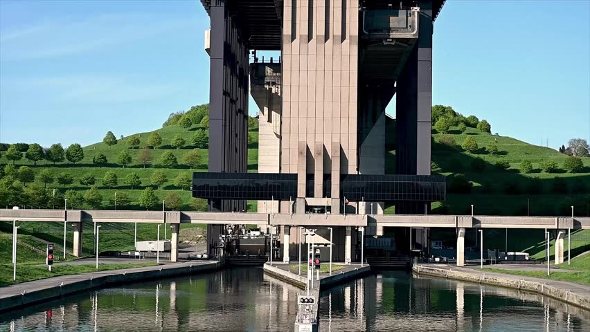 Static close-up view of canal boat lift lock gates slowly closing after a barge has entered the caisson chamber. The hydraulic mechanism seals the water-tight compartment with heavy steel gates sliding into position between concrete walls. Detailed view of the gate closure process showing engineering precision and industrial scale of the lock mechanism that must contain thousands of cubic meters of water during the lifting operation. Lock gate closing mechanism, boat lift caisson being sealed, hydraulic gate engineering detail.