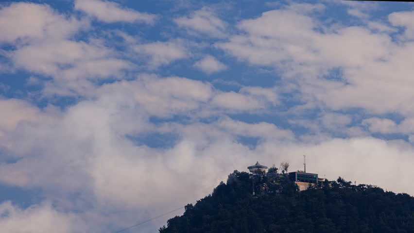 Clouds moving above a mountain peak and hilltop structure.