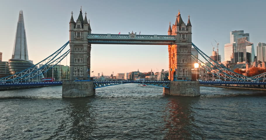Tower Bridge standing over River Thames with The Shard and other modern skyscrapers in London skyline during a golden hour sunset, showing iconic British architecture at dusk. Aerial view drone flight