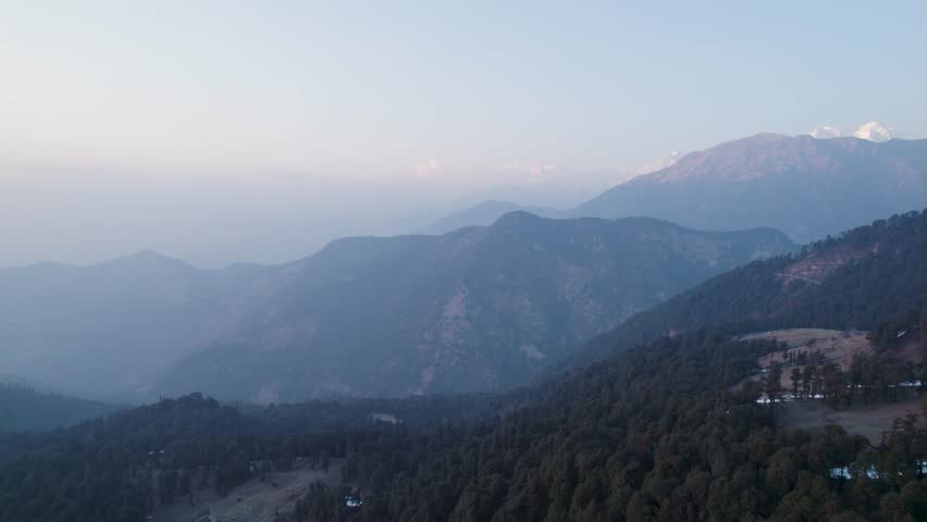 Aerial view of Chopta Tungnath with misty mountain ridges and dense evergreen forests under a soft morning sky in Chopta, Uttarakhand, India.