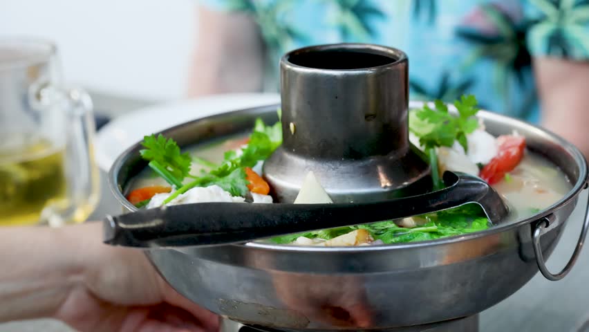 Close-up shot of steaming spicy seafood soup served in a traditional metal hot pot bowl