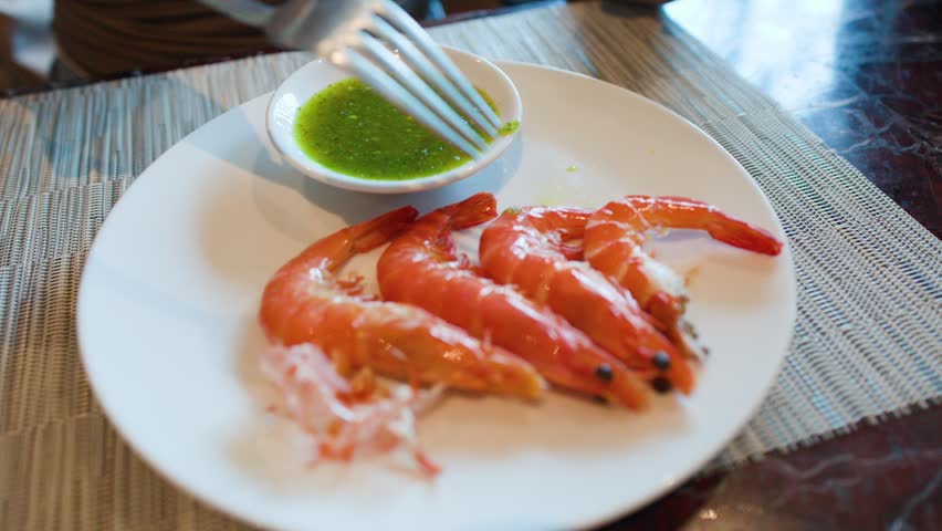 A fork dips a large grilled shrimp into a bowl of spicy green seafood sauce