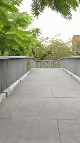 A slow panning shot follows a modern concrete elevated walkway surrounded by tropical green foliage
