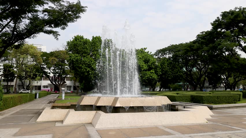 A wide shot captures a tiered water fountain spraying upwards in a peaceful university park