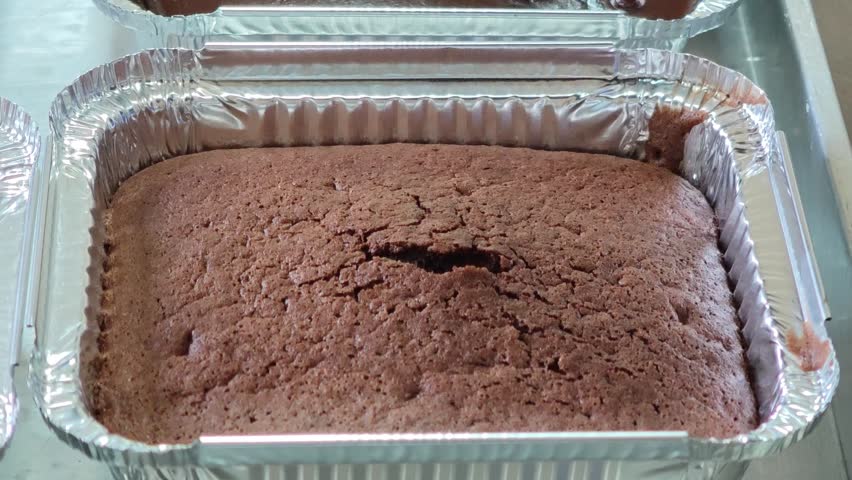 The chocolate cake is being topped with frosting.