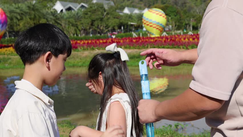 Young girl learns to blow soap bubbles with father and brother in sunny lakeside park