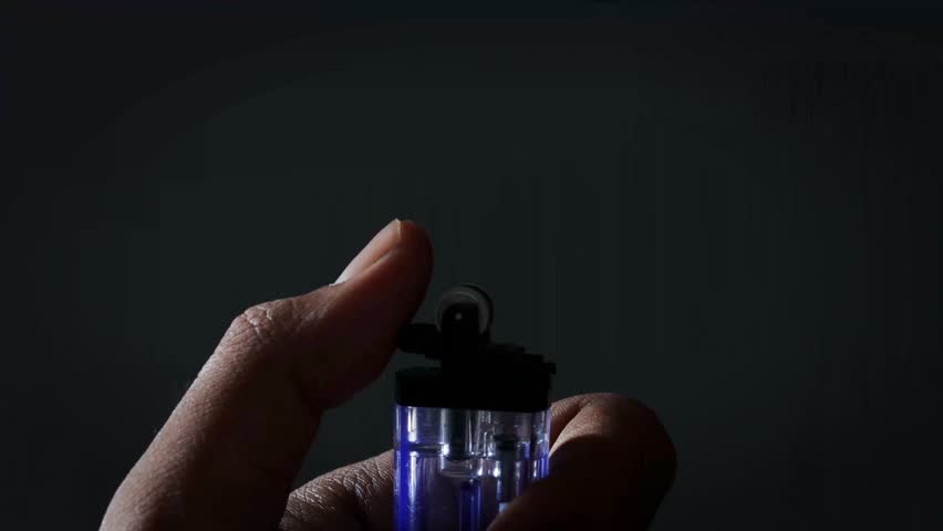 A man lights a lighter. A man holds a lighter in his hand and spins a drum on a dark background. The lighter emits sparks and ignites close up.