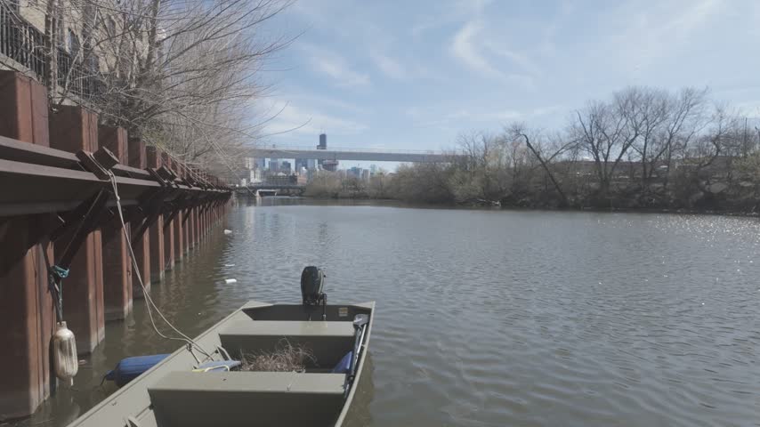 A boat tied up to a river wall on the Chicago River with the Chicago skyline in the background on a sunny day.