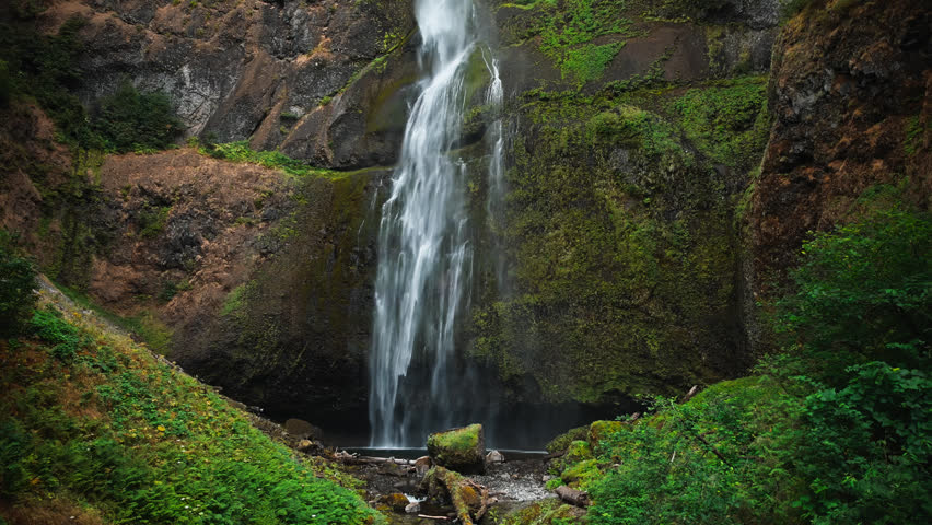 Close details of Multnomah Falls upper falls flowing over mossy rocks into pool below