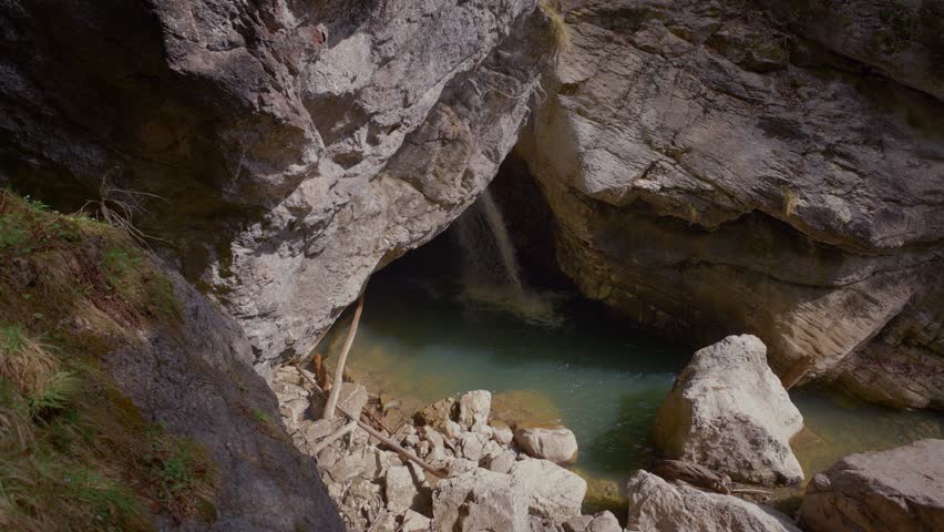 Clear turquoise mountain water in a rock pool, waterfall from a dark cave opening. Starzlachklamm gorge