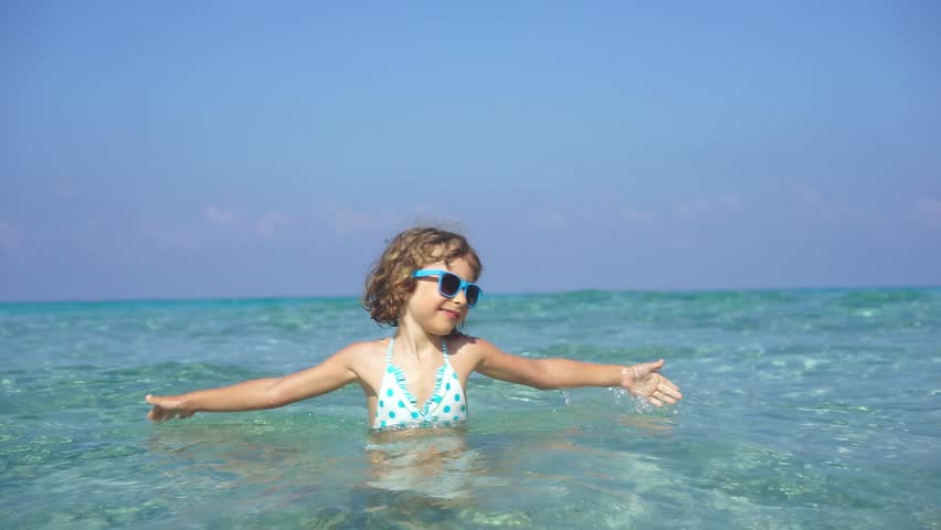A happy child is having fun at the beach during the summer holidays. Funny girl enjoying a vacation in the sea. Slow motion
