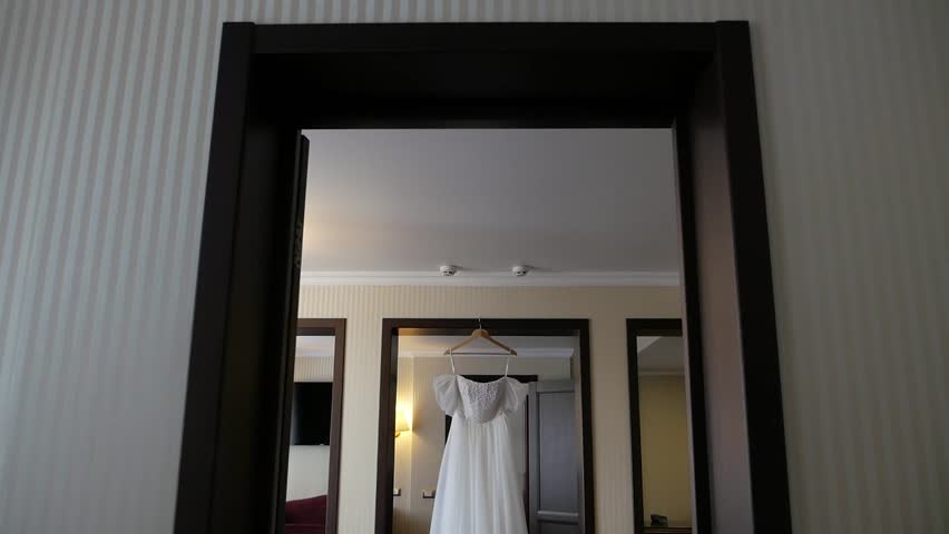 A white wedding dress is hanging on a hanger in the doorway. Wedding morning.