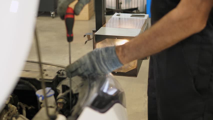 A close-up of a worker checking and adjusting the headlights of a car