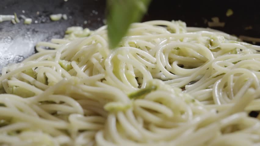 Close view of spaghetti pasta cooking in creamy sauce while being stirred inside kitchen pan during food preparation in Mexico kitchen.