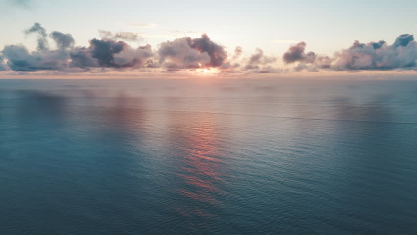 Aerial high altitude view of the Atlantic Ocean surface during calm sunrise with some clouds in the sky