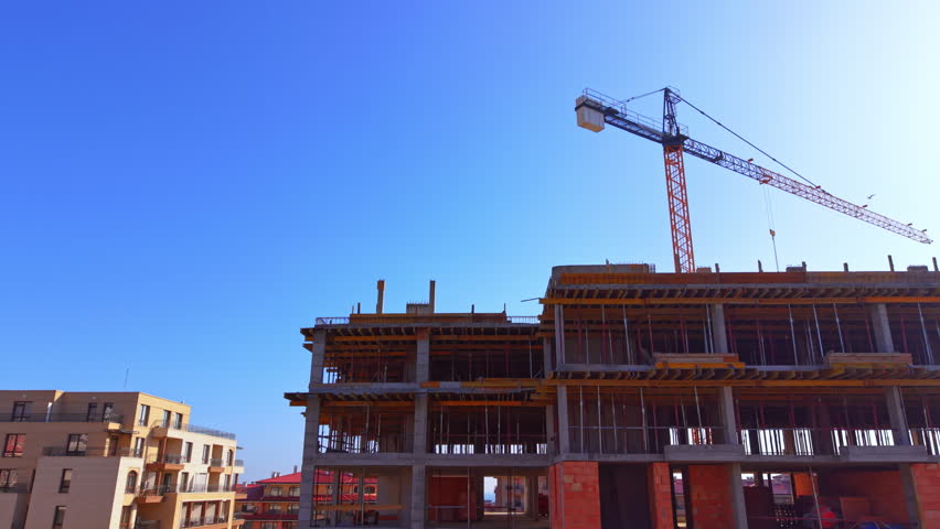 Looking up at a residential structure under development showcasing scaffolding poles and orange brickwork. Aerial view of tower crane above concrete building frame