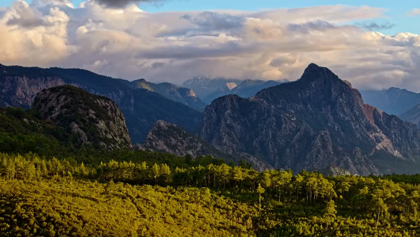 Cinematic aerial view of a dark mountain valley, reflective lake waters, dramatic clouds, and golden sun rays. Ideal for travel, nature, adventure, tourism, and outdoor landscape themes.
