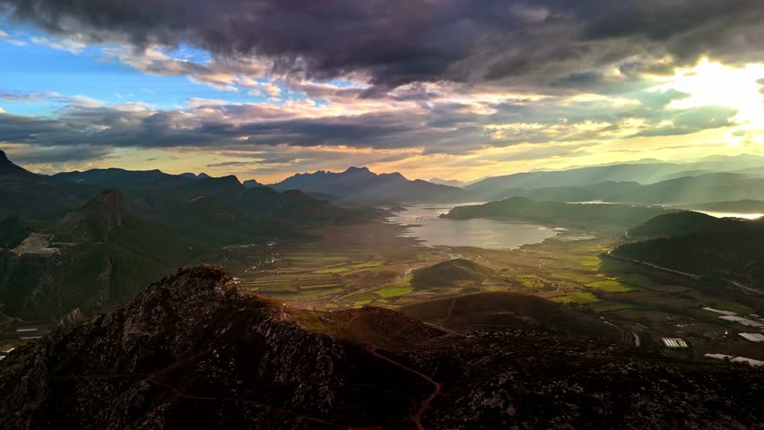 Cinematic aerial view of a wide mountain valley, calm lake, golden sunset light, and dramatic clouds. Ideal nature background for travel, adventure, tourism, hiking, and outdoor themes.