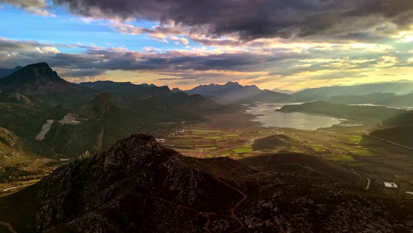 Cinematic aerial view of a wide mountain valley, calm lake, golden sunset light, and dramatic clouds. Ideal nature background for travel, adventure, tourism, hiking, and outdoor themes.