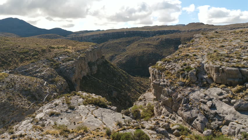 Cinematic drone footage of person riding zipline across rocky canyon in Malargüe, Mendoza province, Argentina.