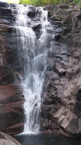 Couple from behind, man and woman embracing and holding hands while looking at a powerful forest waterfall in Norway. Romantic adventure and sustainable travel concept in Northern Europe.