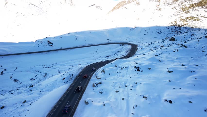 Cars driving on a winding Julier Pass road through a snow covered Alpine landscape in winter