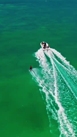  A drone view of a guy skiing behind a speedboat on crystal-clear water. Extreme sports, recreational activities