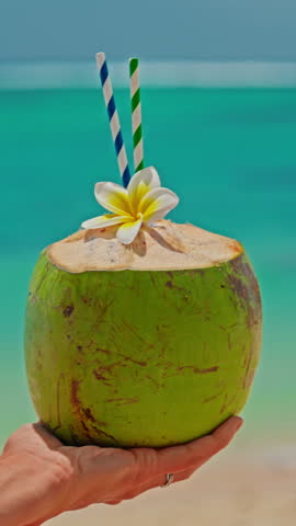 A close-up portrait of a woman drinking a fresh coconut cocktail with turquoise water on the shore of the Indian Ocean. A smile on the face. Positive emotions. Concept of relaxation and travel