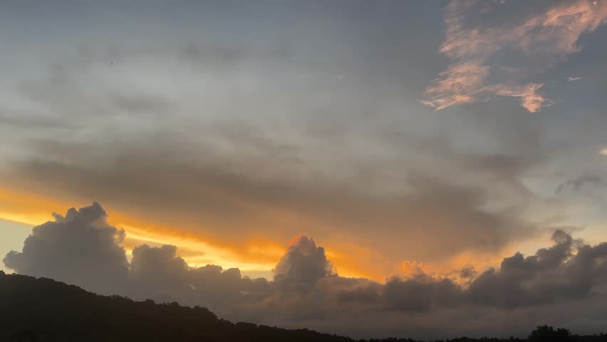 Stunning 4k footage capturing a dramatic sunset with vibrant golden and orange light glowing behind dark cumulus clouds